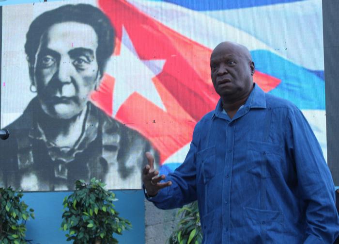 El actor Jorge Ryan habla sobre Mariana Grajales, al fondo imagen su imagen y la bandera cubana